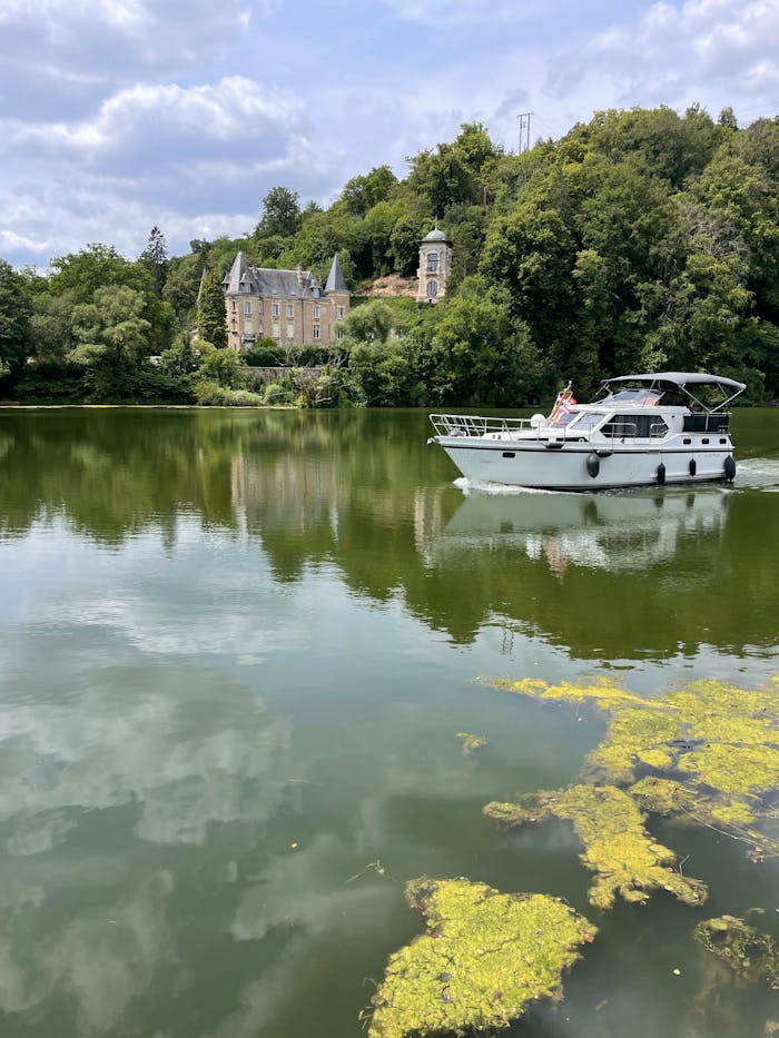 A tranquil river scene with a yacht near a castle in France, surrounded by lush greenery.